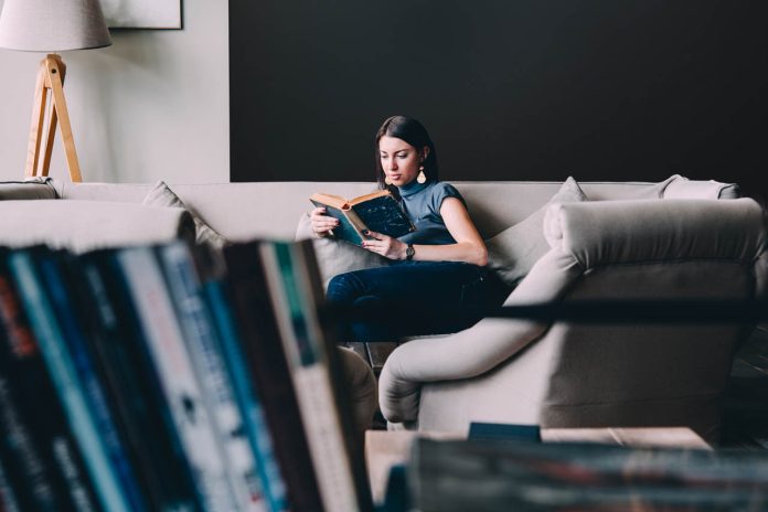 Young,Beautiful,Woman,Enjoys,Reading,Sitting,On,A,Comfortable,Couch.